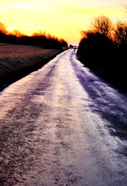 Bir eğrisi sağa, Frost'un üzerinde yol ve kırsal, gökyüzünde yükselen kırmızı şafak ışığı ile bir ülke şeritli