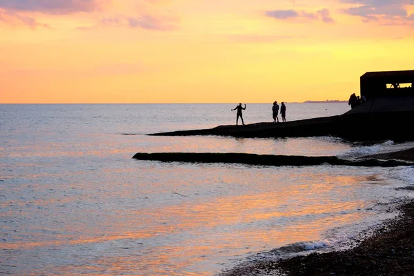 海堤在日落在布赖顿海滩 跳船是 Silhoutted 黑由明亮的橙色和黄色焕发日落 在跳船是一群青少年演奏 他们是 Silhoutted 由太阳 因此是黑色人的形状移动 — 图库照片