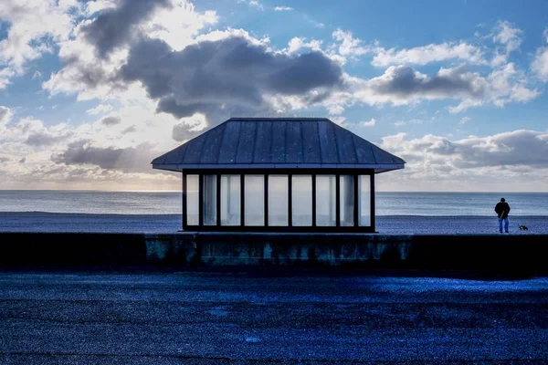一个现代化的玻璃和金属座椅在卵石滩 海背后的照片和一个多云对比天空的前景是柏油线 图像具有图形形状的外观 — 图库照片