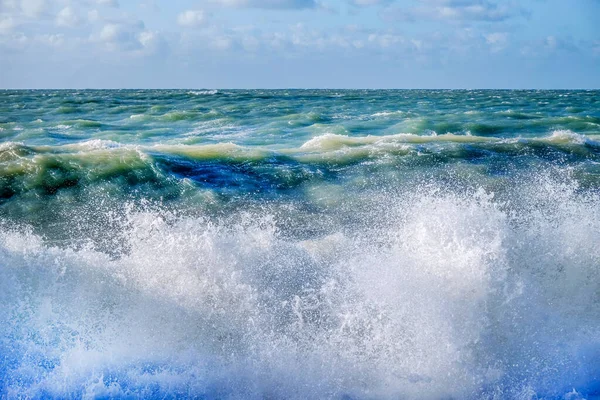 Rocío de mar blanco de una ola rompiendo en la playa con un mar agitado —  Fotos de Stock