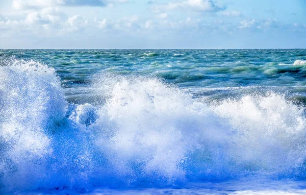 Rocío blanco de una ola rompiendo en la playa con un mar agitado y —  Fotos de Stock