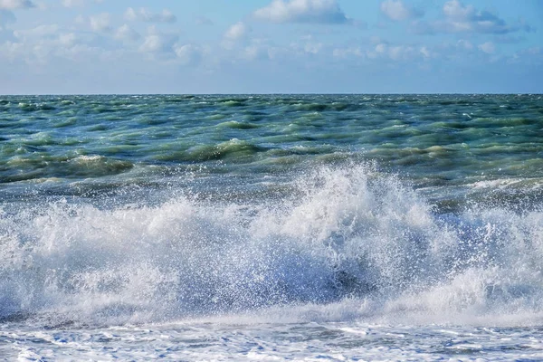 Rocío blanco de una ola rompiendo en la playa con un mar agitado y —  Fotos de Stock