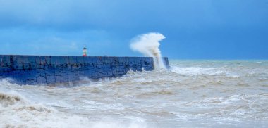 A harbour wall with a rough sea crashing against it and a lighth clipart