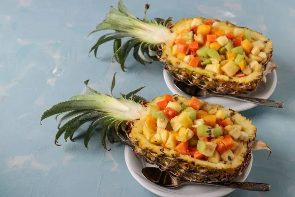 Tropical fruit salad in pineapple halves on a light blue background, Copy space