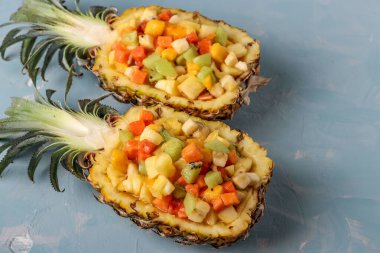 Açık mavi arkaplanda ananas yarılarında tropik meyve salatası, yatay yönelim