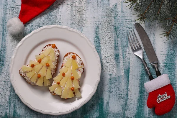 Neujahrssandwiches mit Käse, Ananas und Krabbenstichen in Form eines Weihnachtsbaums, dekoriert mit Sanddornbeeren, liegen auf einem weißen Teller, Draufsicht — Stockfoto