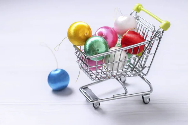 Trolley cart and colorful new year balls on white background, creative flat lay shopping, Copy space — Stock Photo, Image