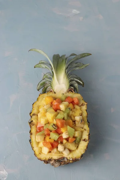 Tropical fruit salad in pineapple halves on a light blue background, Top view, vertical orientation — Stock Photo, Image