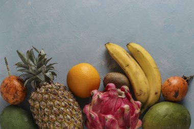 Taze tropikal meyveler: mango, ananas, ejderha, kivi, muz, turuncu ve tutku meyveleri açık mavi arka planda, yatay yönelim