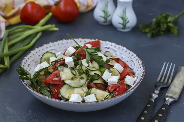 Здоровий салат з кабачками, помідорами та фетою, одягнений в оливкову олію в тарілку на темному фоні, горизонтальна орієнтація — стокове фото