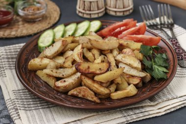 Koyu arkaplanda domates, salatalık ve maydanozla servis edilen fırında patates.