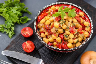 Biber ve domatesli nohut garnitürü. Protein açısından zengin bir vejetaryen yemeği. Yatay olarak koyu bir arka planda yer alıyor.
