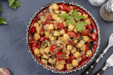 Biber ve domatesli nohut garnitürü. Protein açısından zengin bir vejetaryen yemeği. Yatay olarak koyu bir arka planda yer alıyor.