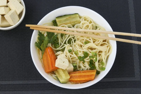 Supă asiatică tradițională cu brânză tofu, tăiței, morcovi și dovlecei pe fundal întunecat, Acest fel de mâncare conține de obicei bouillon și legume, Vedere de sus — Fotografie, imagine de stoc