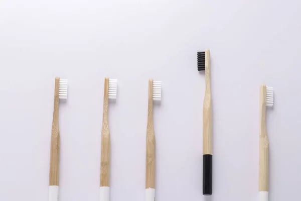 Une brosse à dents éco noire s'envole des autres brosses à dents blanches sur fond mural blanc. Unique, penser différemment, individuel et se démarquer du concept de foule — Photo