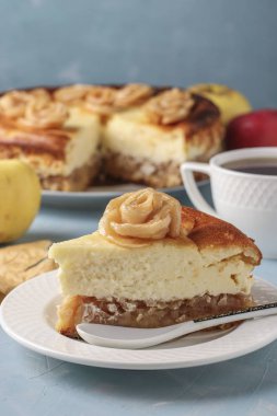 Açık mavi arkaplanda elmalı cheesecake, elma ve fincandan güllerle süslenmiş, dikey oryantasyon