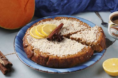 Limonlu, tarçınlı ve cevizli ev yapımı balkabağı turtası, hindistan cevizi serpilmiş, dilimlenmiş, açık mavi arka planda bir fincan kahveyle
