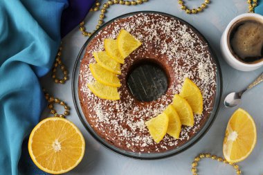 Ortasında delik olan portakallı ev yapımı kek, açık mavi arka planda hindistan cevizi taneleri serpiştirilmiş ve bir fincan kahve, Top view