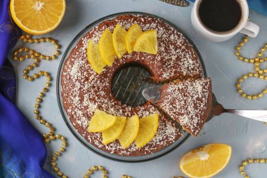 Ortasında delik olan portakallı ev yapımı kek, açık mavi arka planda hindistan cevizi taneleri serpiştirilmiş ve bir fincan kahve, Top view