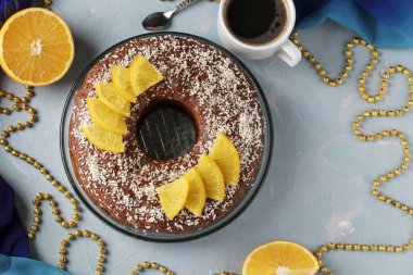 Ortasında delik olan portakallı ev yapımı kek, açık mavi arka planda hindistan cevizi taneleri serpiştirilmiş ve bir fincan kahve, Top view