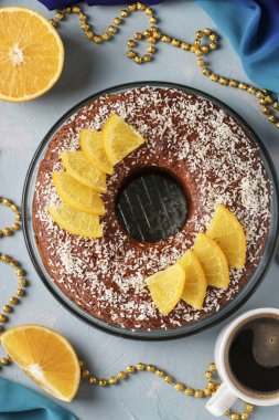 Ortasında delik olan portakallı ev yapımı kek, açık mavi arka planda hindistan cevizi taneleri serpiştirilmiş ve bir fincan kahve, Top view