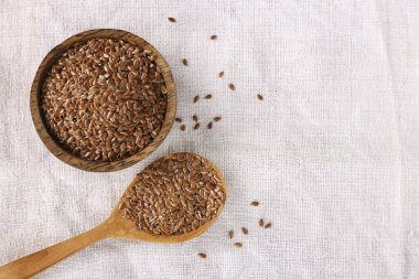 Tahta bir kaşıkta keten tohumu ve doğal keten bir masa örtüsü üzerinde kase, kopyalama alanı, üst görünüm.