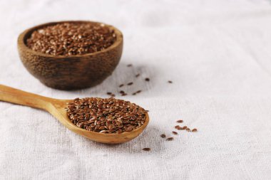 Tahta bir kaşıkta keten tohumu ve doğal keten bir masa örtüsü üzerinde kâse, boşluğu kopyala.