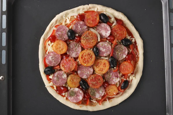 Pizza cu cârnați, roșii, mozzarella și măsline pe o tavă de copt înainte de coacere — Fotografie, imagine de stoc