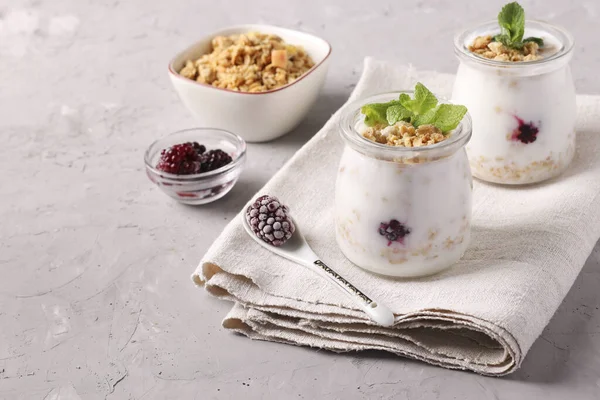 格拉诺拉甜甜蜜蜜与天然酸奶 冰冻的浆果和薄荷在玻璃瓶灰色背景 健康的食物 复制空间 — 图库照片