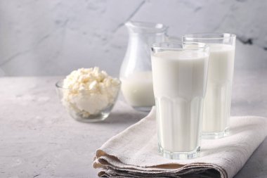 Kefir ya da Ayran bardakta mayalanmış içkinin yanı sıra açık gri arka planda bir kasede süzme peynir. Boşluğu kopyala, kapat.