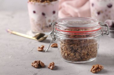 Çikolatalı gevrek müsli, doğal bal ve fındıklı cam kavanozda gri arka plan, sağlıklı yemek, yakın çekim.