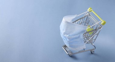 Koruyucu maskeli market arabası Coronavirus salgını sırasında alışveriş yapma tehlikesi kavramı COVID-19.