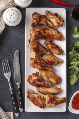 Beyaz tabakta ızgara tavuk kanadı ve koyu arka planda domates sosu, yakın plan, üst manzara.