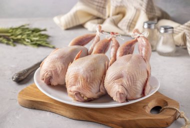 Tahta üzerinde beyaz bir tabakta üç taze bıldırcın.