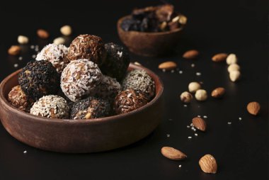 Fındık topları, yulaf ezmesi ve kurumuş meyveler kahverengi bir tabakta siyah arka planda, yatay formatta, yakın plan