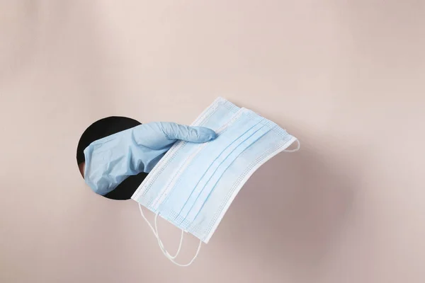 La mano femenina en un guante sostiene dos máscaras médicas protectoras a través de un agujero redondo en papel rosa — Foto de Stock