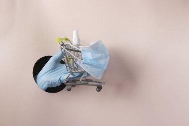 Kadın el arabası koruyucu maske takıyor ve elleri için antiseptik kullanıyor pembe kağıttaki yuvarlak delikten Coronavirus salgını sırasında alışveriş yapma tehlikesi kavramı COVID-19, kopyalama alanı.