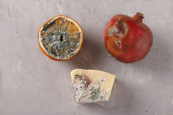 Spoiled rotten foods with mold: half an orange, pomegranate and hard cheese on gray background, Top view