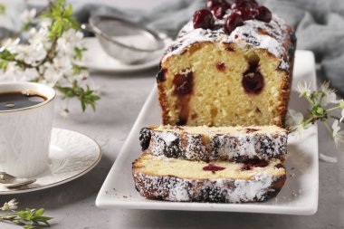 Gri beton arka planda beyaz bir tabağa yerleştirilmiş kirazlı kek ve bir fincan kahve, yatay format, yakın plan.