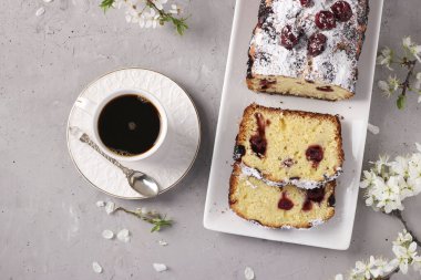 Kirazlı kek, gri beton zemin üzerinde beyaz bir tabakta ve bir fincan kahve, yatay format, yukarıdan görünüm