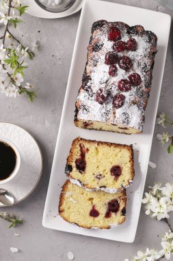 Kirazlı kek gri beton arka planda beyaz bir tabakta ve bir fincan kahve, dikey format, yukarıdan görünüm