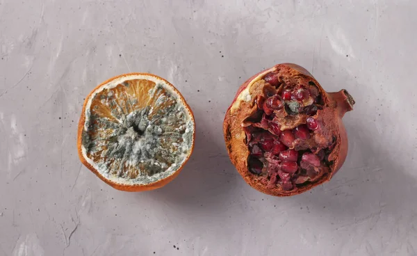 Spoiled rotten foods with mold: half an orange and pomegranate on gray background, Top view, Closeup