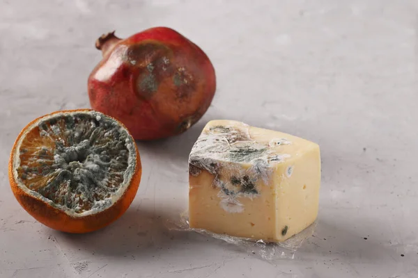 Spoiled rotten foods with mold: pomegranate, half an orange and hard cheese on gray background, Closeup