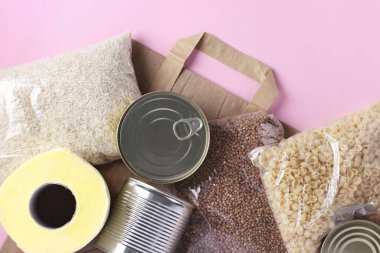 Pembe arka planda karantina süresi için gıda stokları içeren kağıt torba. Pirinç, karabuğday, makarna, konserve yiyecek, tuvalet kağıdı. Yemek teslimatı, Bağış, Üst Manzara, Yakın Çekim