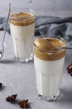 Açık gri arka planda çırpılmış köpüklü bir bardakta Dalgona kremalı kahve. Kore kahve eğilimi, Yakın plan, Dikey Biçim