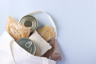 Gıda tedarikli Tekstil Market Torbası açık mavi arka planda karantina izolasyon dönemi için gıda stoku krizine girdi. Pirinç, karabuğday, makarna, konserve yiyecek. Gıda teslimatı, Bağış, Kopyalama alanı