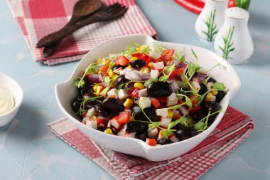 Siyah fasulyeli salata, mısır, yengeç çubuğu ve bezelye mikrogreni açık mavi arka planda beyaz bir kasede, yakın plan