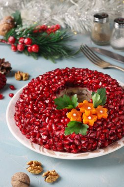 Nar tohumlarıyla süslenmiş salata narlı bileziği ve açık mavi arka planda havuç çiçekleri. Geleneksel Rus Yeni Yıl Salatası, Yakın plan, Dikey Biçim