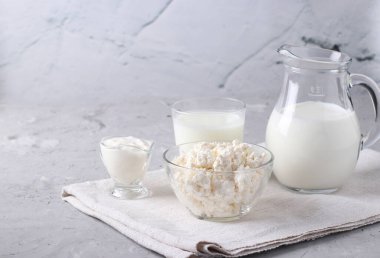 Süt ürünleri: süt, kefir veya ayran, şeffaf bir kasede süzme peynir ve ekşi krema, gri bir arka planda sürahi ve cam, metin için yer