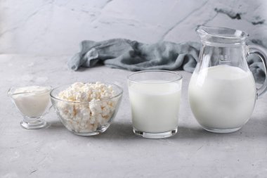 Süt ürünleri: süt, kefir veya ayran, süzme peynir ve ekşi krema şeffaf bir kase içinde, sürahi ve cam gri arka planda, yatay format